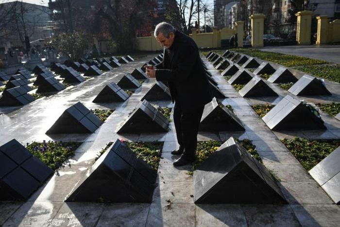 Ioan Banciu lights a candle next to the empty tomb of his wife, one of the victims of the Romanian revolution