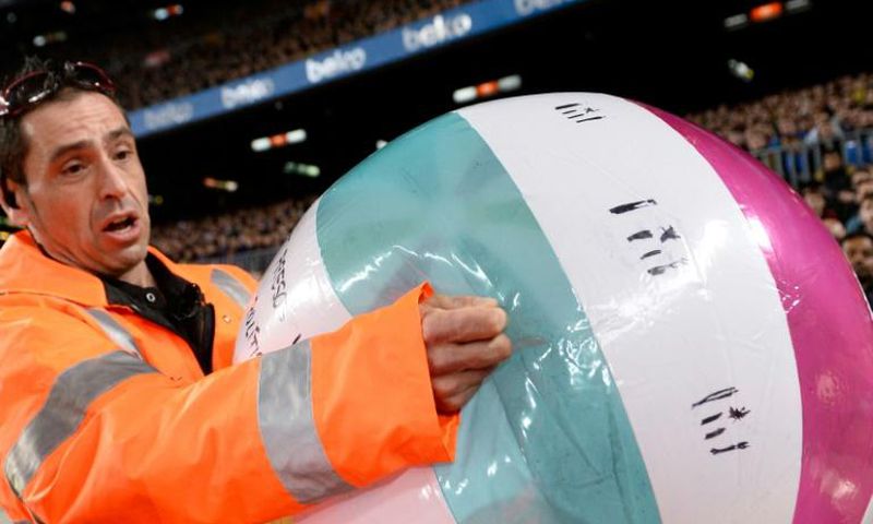 A staff member removes an inflatable ball thrown by Barcelona supporters on to the pitch
