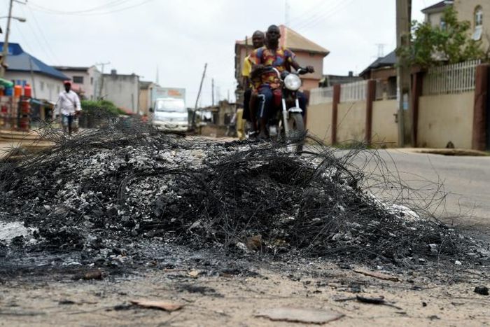 A motorcycle taxi in the district of Ojodu drives past the remains of a fire set to ward off gangs of robbers