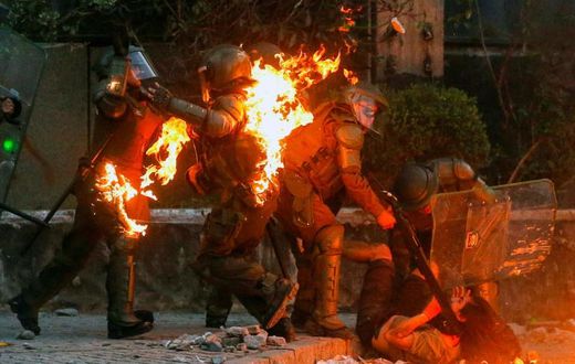 A demonstrator is held while a petrol bomb hits riot police during a protest against the government in Santiago on Friday
