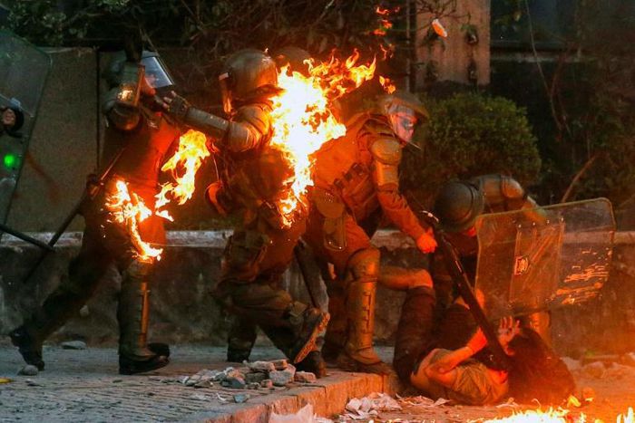 A demonstrator is held while a petrol bomb hits riot police during a protest against the government in Santiago on Friday