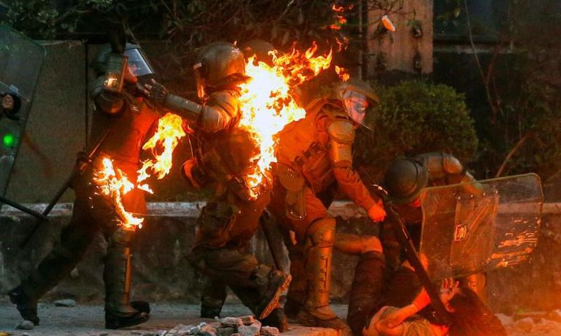A demonstrator is held while a petrol bomb hits riot police during a protest against the government in Santiago on Friday