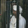 Sudan's deposed military ruler Omar al-Bashir stands in a defendant's cage at the opening of his corruption trial in Khartoum in August