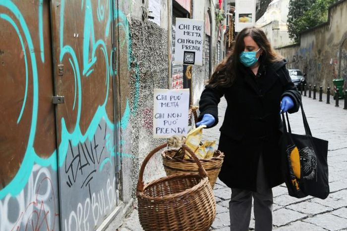 A woman puts food in a solidarity basket displayed with a note reading, "Who can put, who cannot take" in Naples, as Italy sees evidence it may have made it through the worst of the coronavirus pandemic