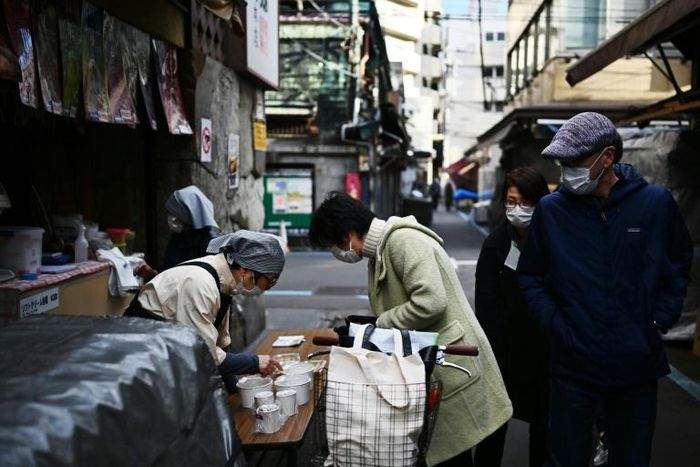 A woman in a face mask buys food from a vendor in Tokyo