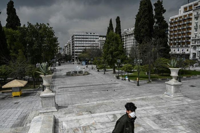 A man wearing a protective face mask walks at empty Athens' empty Syntagma square on March 23, 2020 as the country struggles to control the spread of the COVID-19, the novel coronavirus