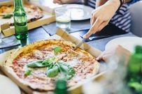 Hand cutting pizza in box on table