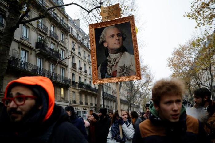 A protester holds a portrait of French President Emmanuel Macron painted as a royalty with a sign on top of it reading "14 May 2017 restoration of the monarchy"