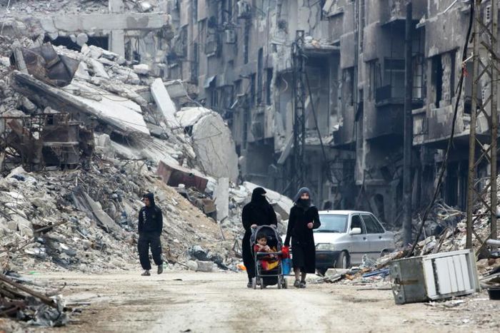 Syrian civilians walk thorugh the former rebel-held town of Harasta in Eastern Ghouta on March 30, 2018, a week after regime forces retook the town