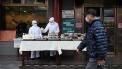 Restaurant workers wear protective clothing as they prepare food to sell on the street outside their restaurant in Beijing