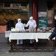 Restaurant workers wear protective clothing as they prepare food to sell on the street outside their restaurant in Beijing