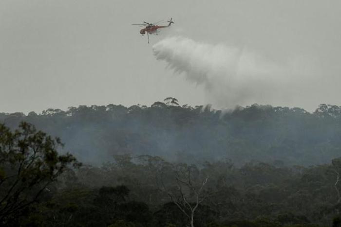 A helicopter dumps water on a bushfire in the outer suburbs of Melbourne