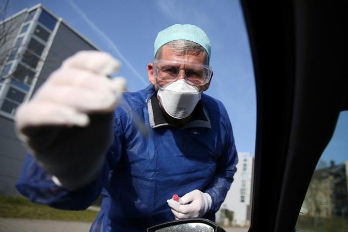 German doctor Michael Grosse takes a sample from a car driver at a drive-through testing point for the coronavirus in Halle, eastern Germany