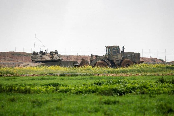 An Israeli tank and a bulldozer are seen along the border fence between Israel and the Gaza Strip where the army says troops shot dead a Palestinian suspected of placing a bomb near the barrier
