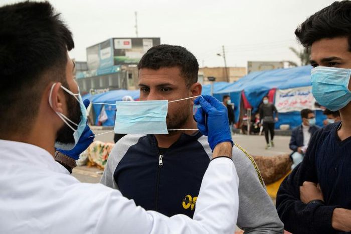 An Iraqi student shows an anti-government demonstrator how to wear a protective mask against the coronavirus during a rally in the southern Iraqi city of Basra