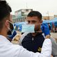 An Iraqi student shows an anti-government demonstrator how to wear a protective mask against the coronavirus during a rally in the southern Iraqi city of Basra
