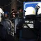 Greek riot police officers watch migrants acrss the barbed wire border