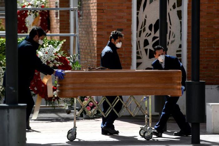 Mortuary employees wearing face masks wheel a coffin into the crematorium at  La Almudena cemetery in Madrid on Tuesday