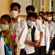 Masked Cambodian students line up to disinfect their hands with an alcohol solution before entering class at a school in Phnom Penh