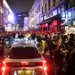 A car tries to drive along a street filled with people drinking in the Soho area of London