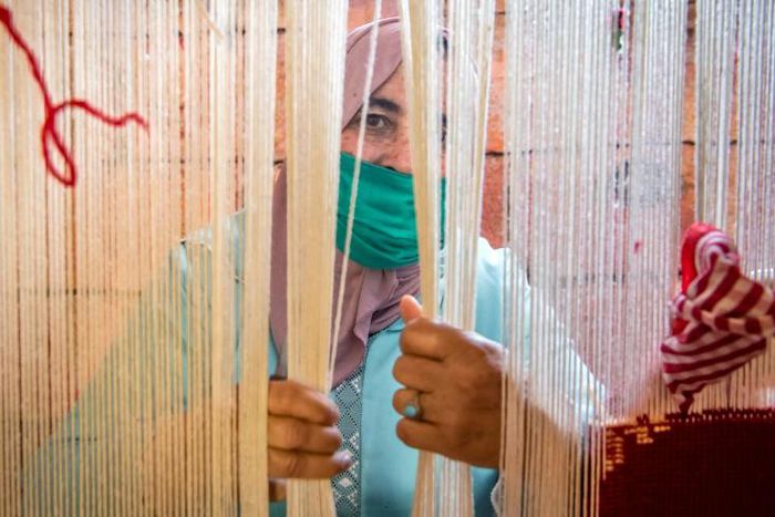A Moroccan rug weaver peeks from behind carpet thread at a workshop in the city of Sale, north of the capital Rabat