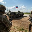 US soldiers stand along the side of a road across near a Russian military armoured personnel carrier (APC), near the village of Tannuriyah in the countryside east of Qamishli in Syria's northeastern Hasakah province on May 2, 2020