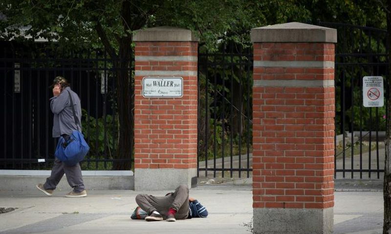 A pedestrian walks past a passed-out drug user on June 25, 2020 in Ottawa, Canada; an emergency government pandemic payment has been used by some addicts to buy drugs, and overdoses have surged