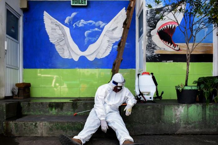 An Indonesian health agency official rests at the entrance to a public toilet as other colleagues conduct COVID-19 testing in Bandung, West Java