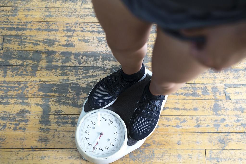 Low section of man checking weight on scale in gym