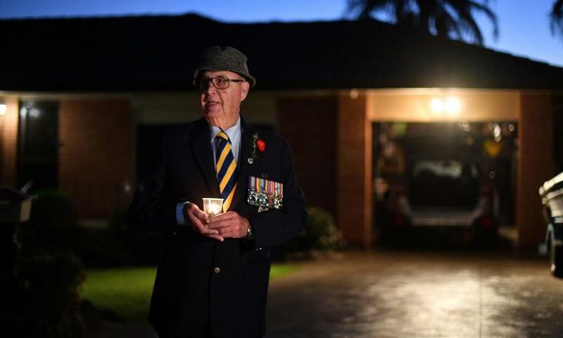 Veteran Peter McFarlane holds a candle during an Anzac Day dawn vigil outside his house in suburbs of Sydney