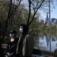 The Midtown Manhattan skyline is reflected in the water as people in masks walk along the lake in Central Park