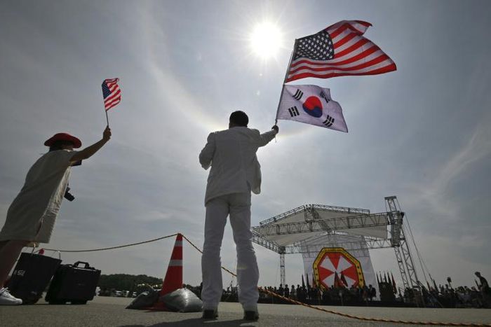 A man and a woman wave flags during a ceremony at the US Camp Humphreys in Pyeongtaek in June, 2019