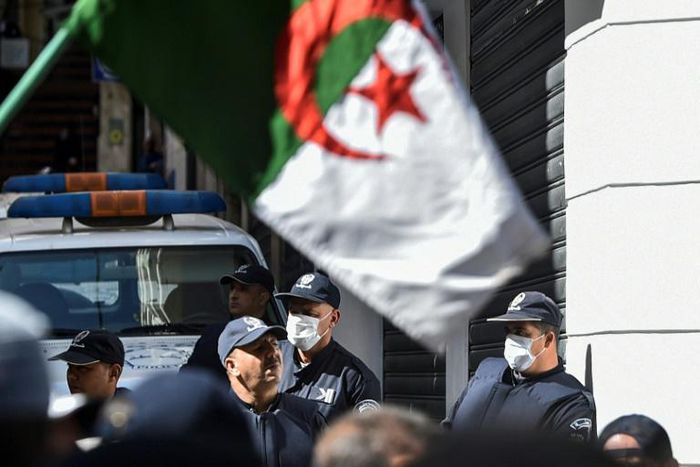 Algerian police wearing face masks stand as protesters march past during an anti-government demonstration in the capital Algiers on March 6