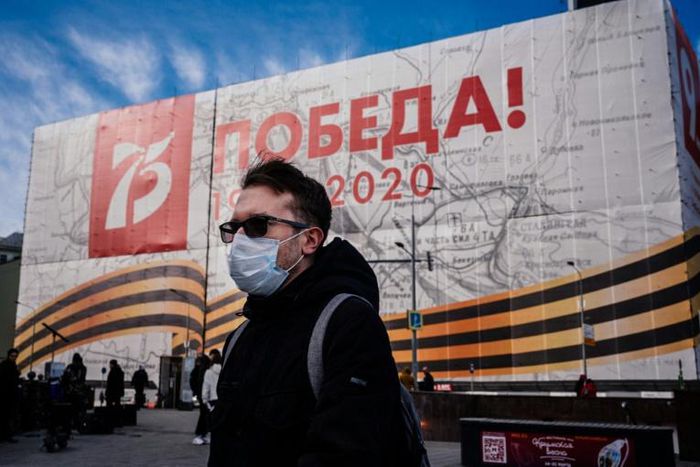 A man wearing a face mask against the spread of the coronavirus walks past a banner for the now much reduced 75th anniversary celebrations in Moscow marking  the victory over Nazi Germany in World War II