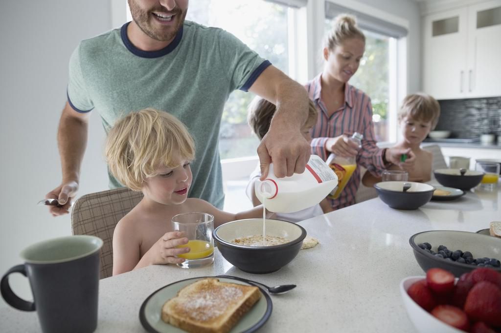Father pouring milk into cereal for son at breakfast