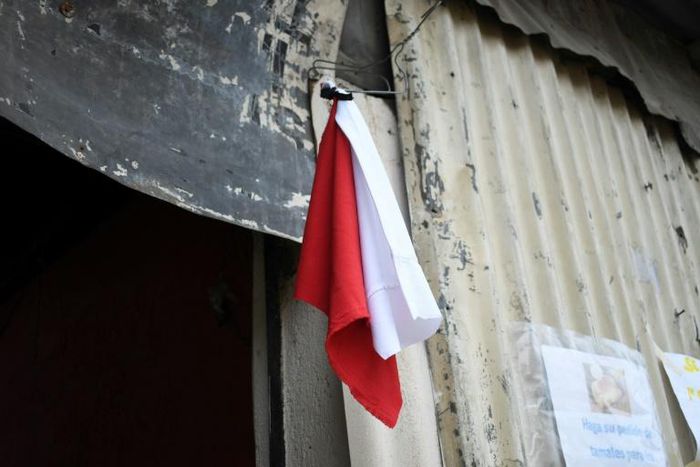 A woman hangs colored flags on the door of her house to signal she needs to be delivered food (white) and medicine (red) for her sick husband, at La Brigada neighbourhood in Guatemala City