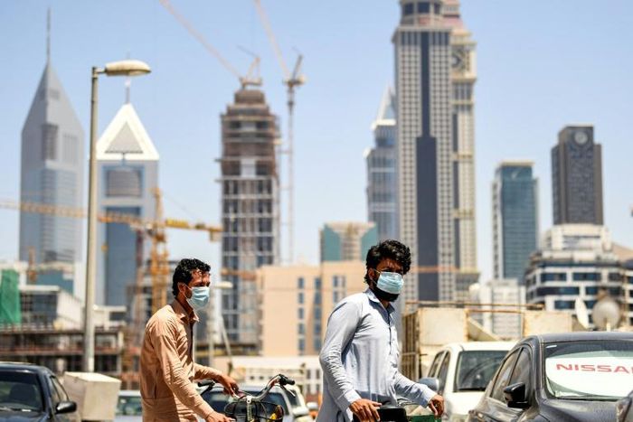 Foreign workers clad in masks to protect against coronavirus push bicycles along a street in the Satwa district of Dubai