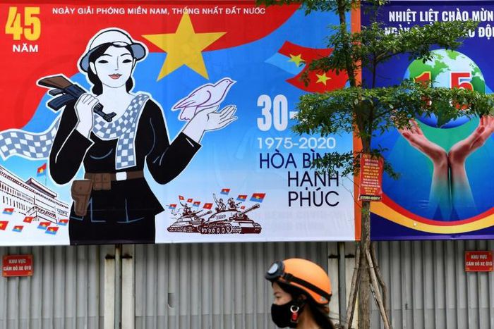 A woman walks next to a hoarding marking the 45th anniversary of the fall of Saigon, in Hanoi