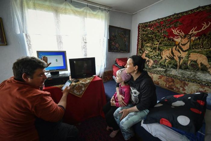 Lucian Cojocaru, a volunteer from "Casa Buna" (The Good Home) NGO, shows a Romanian schoolgirl and her mother how to use a desktop computer, aiding their access to home schooling during the pandemic