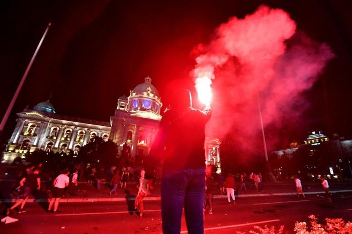 A protestor holds a flare as Serbian police fires tear gas in front of the National Assembly building in Belgrade, on July 7, 2020, to disperse thousands of protesters angry at the return of a weekend coronavirus curfew