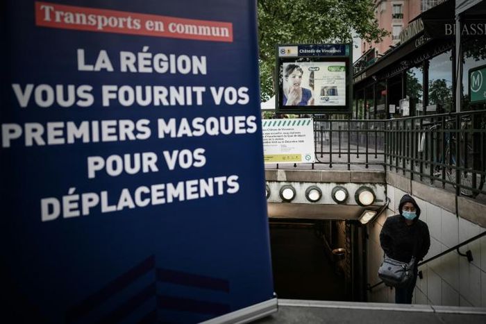 A woman wearing a protective mask walks out of a metro station next to a sign announcing the distribution of face masks to commuters after complaints over shortages of supplies to medical professionals