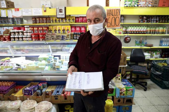 Shop owner Mudaver Uygur shows the book where he notes money owed him by costumers -- wealthier ones have stepped into the breach to pay off debts worth hundreds of dollars in some cases