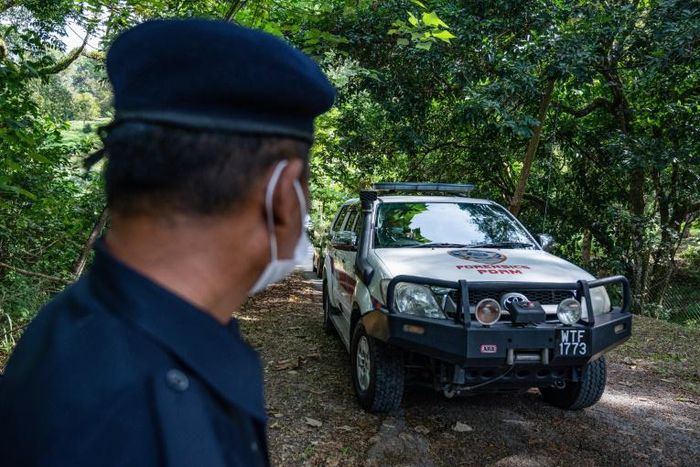 A member of the Royal Malaysia Police stands guard as a forensic vehicle leaves the main entrance of the location where Nora Quoirin's body was found