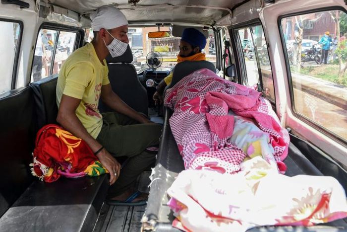 A man sits by the body of a relative who died after apparently drinking toxic moonshine. Dozens of people in Punjab's Tarn Taran district have died after consuming illicit booze in recent days