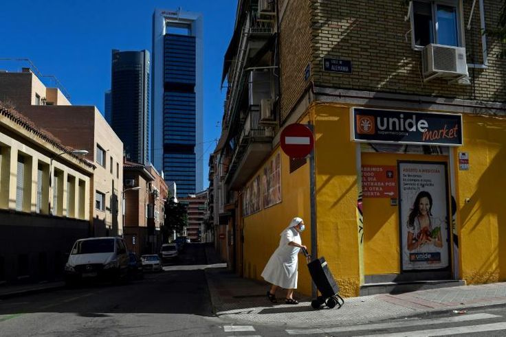 A nun wearing a facemask pushes a trolley in the outskirts of Madrid with the Cuatro Torres business area in the background