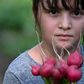 A girl holds a bundle of radishes in the community vegetable garden in El Chaparral