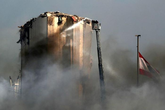 Lebanese firefighters use a ladder to hose down the warehouses and silos of Beirut port after Thursday's blaze