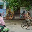 Cyclists ride past the closed gate of a Mumbai movie theatre