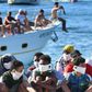 Many migrants land on the holiday destination of Lampedusa island, as sunbathers paddling in crystal waters look on