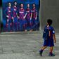 A boy wearing Barcelona's football kit looks at a poster depicting Lionel Messi and other players outside Camp Nou